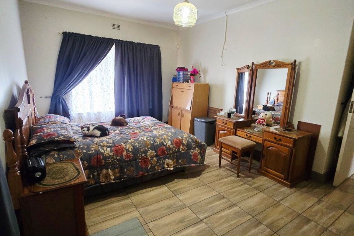 A spacious bedroom featuring tiled flooring, coved ceilings, and a central pendant light fixture, offering a functional layout for a comfortable sleeping area.