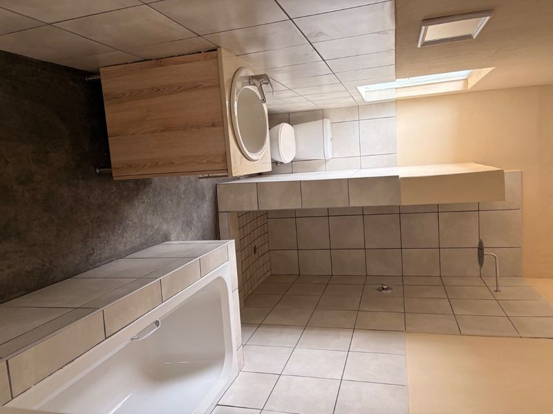 A functional bathroom featuring a built-in bathtub, separate shower area, vanity cabinet with basin, and a skylight for natural illumination.