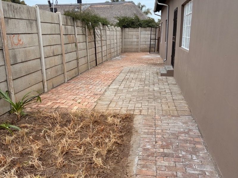 Side exterior area featuring brick paving, a precast concrete boundary wall, and a security gate leading to the main structure.