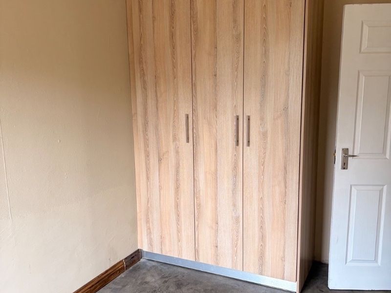 A bedroom featuring a modern light wood-grain built-in wardrobe, polished concrete flooring, and neutral wall tones.