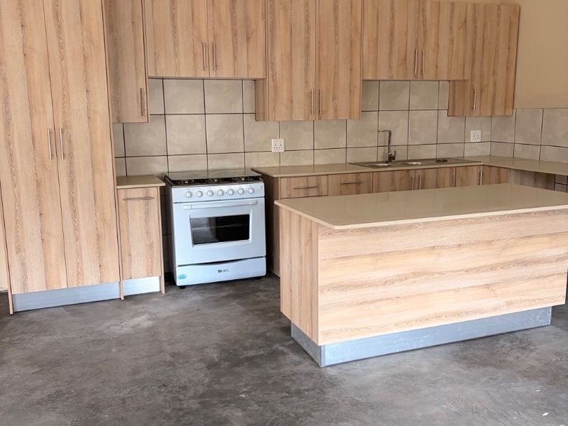 A functional kitchen featuring light wood-look cabinetry, a central island, tiled backsplash, and a freestanding oven, set against an unfinished concrete floor.