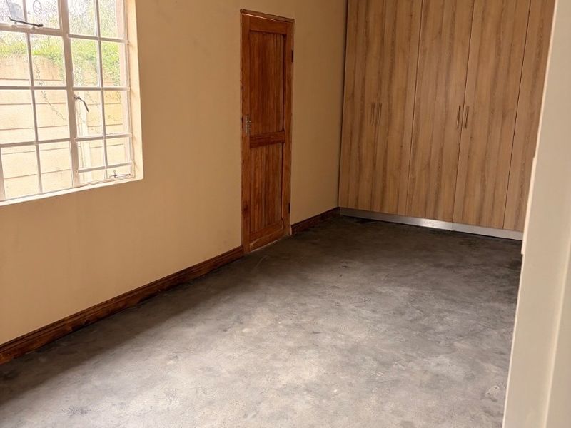 A clean, empty bedroom featuring built-in wooden cupboards, concrete flooring, and a grid-style window, offering a neutral space ready for personalization.
