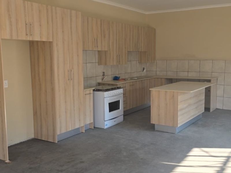A spacious kitchen featuring light wood-look cabinetry, a central island, and a freestanding stove, currently awaiting final flooring installation.