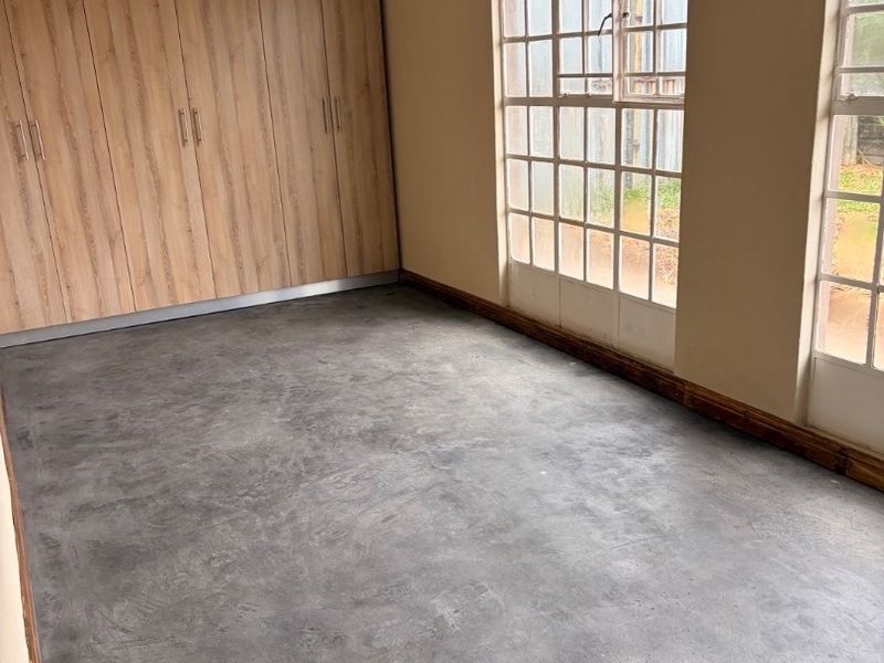 A vacant bedroom featuring built-in wooden cupboards, large grid-pattern windows, and dark grey flooring.