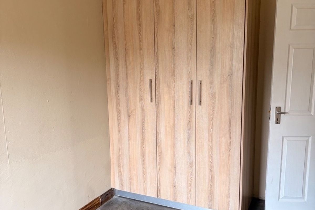 A bedroom featuring a modern light wood-grain built-in wardrobe, polished concrete flooring, and neutral wall tones.