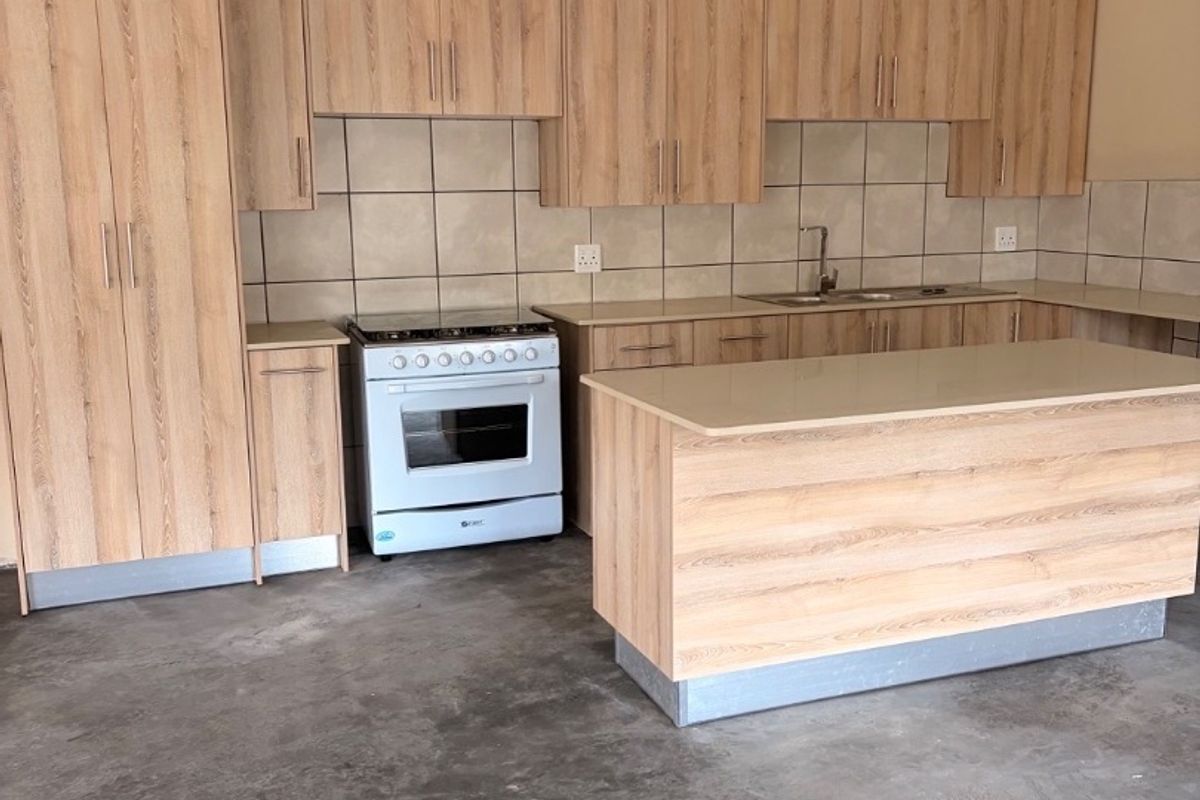 A functional kitchen featuring light wood-look cabinetry, a central island, tiled backsplash, and a freestanding oven, set against an unfinished concrete floor.