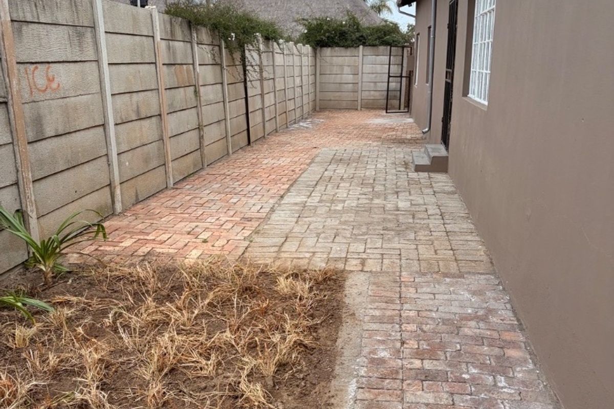 Side exterior area featuring brick paving, a precast concrete boundary wall, and a security gate leading to the main structure.