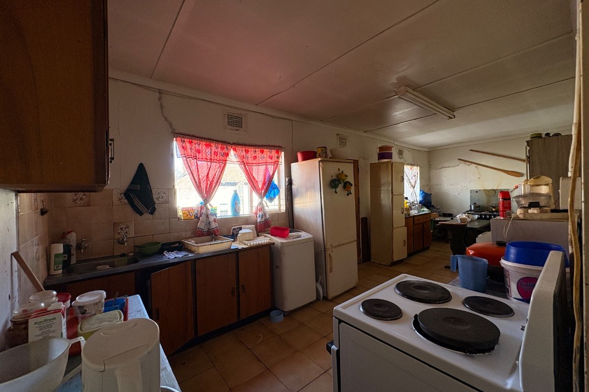 A dated kitchen featuring original cabinetry, tiled splashbacks, and an electric stove, requiring significant renovation and modernization to improve functionality and aesthetic appeal.