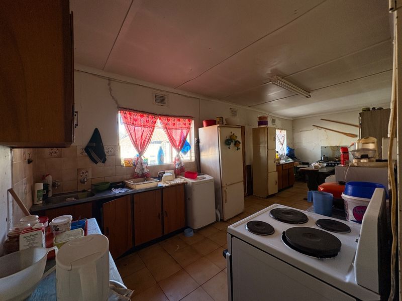 A dated kitchen featuring original cabinetry, tiled splashbacks, and an electric stove, requiring significant renovation and modernization to improve functionality and aesthetic appeal.