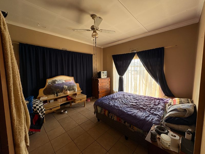 A bedroom featuring tiled flooring and a ceiling fan, currently showing signs of wear including ceiling cracks and peeling paint.