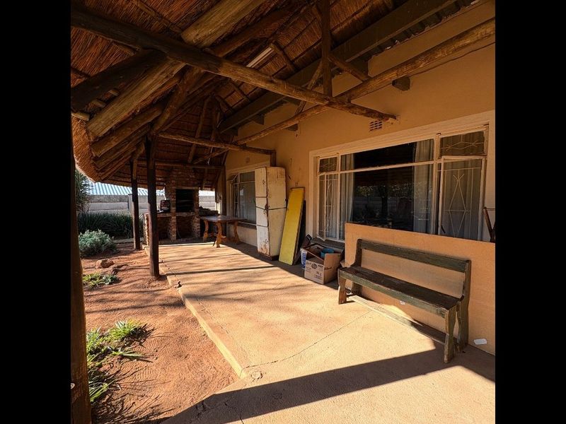 Covered outdoor patio featuring a traditional thatched roof, exposed timber rafters, and a built-in brick braai area, offering potential for an inviting entertainment space.