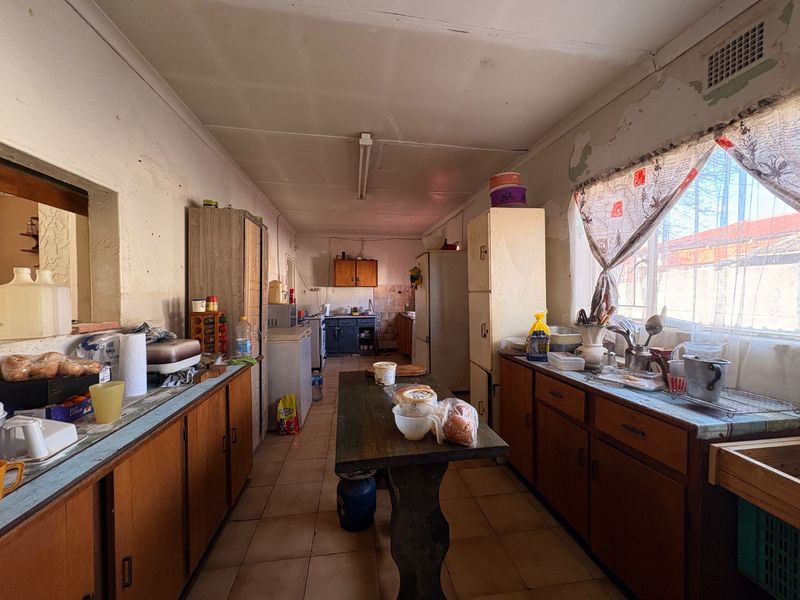 A dated kitchen featuring original built-in cabinetry, tiled flooring, and significant wall surface wear, offering potential for a complete modern renovation.