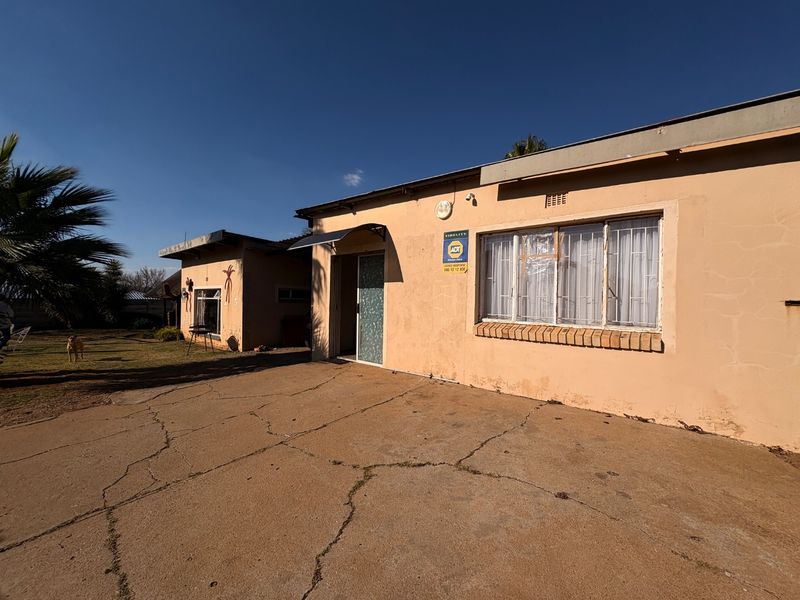 Front exterior view of the house featuring a concrete driveway, security bars on windows, and a brick facade requiring maintenance.