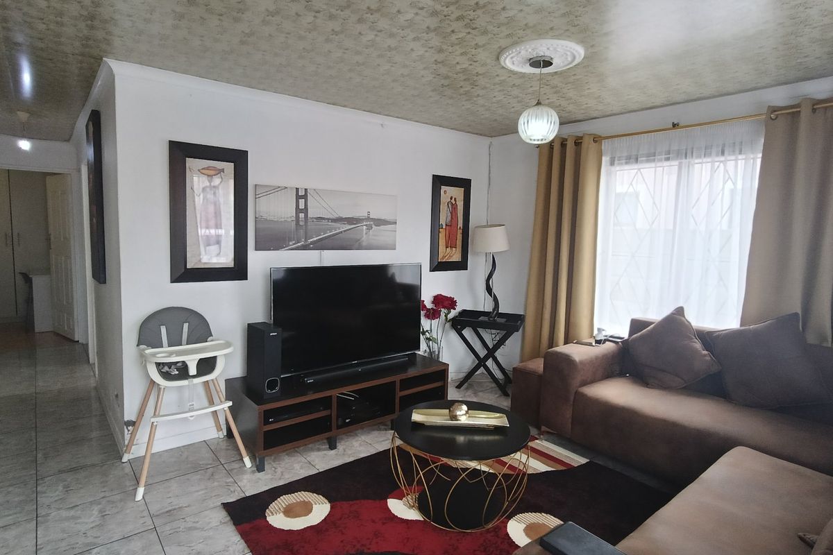 A comfortable living room featuring tiled flooring, a decorative ceiling rose, and a window fitted with a security gate.