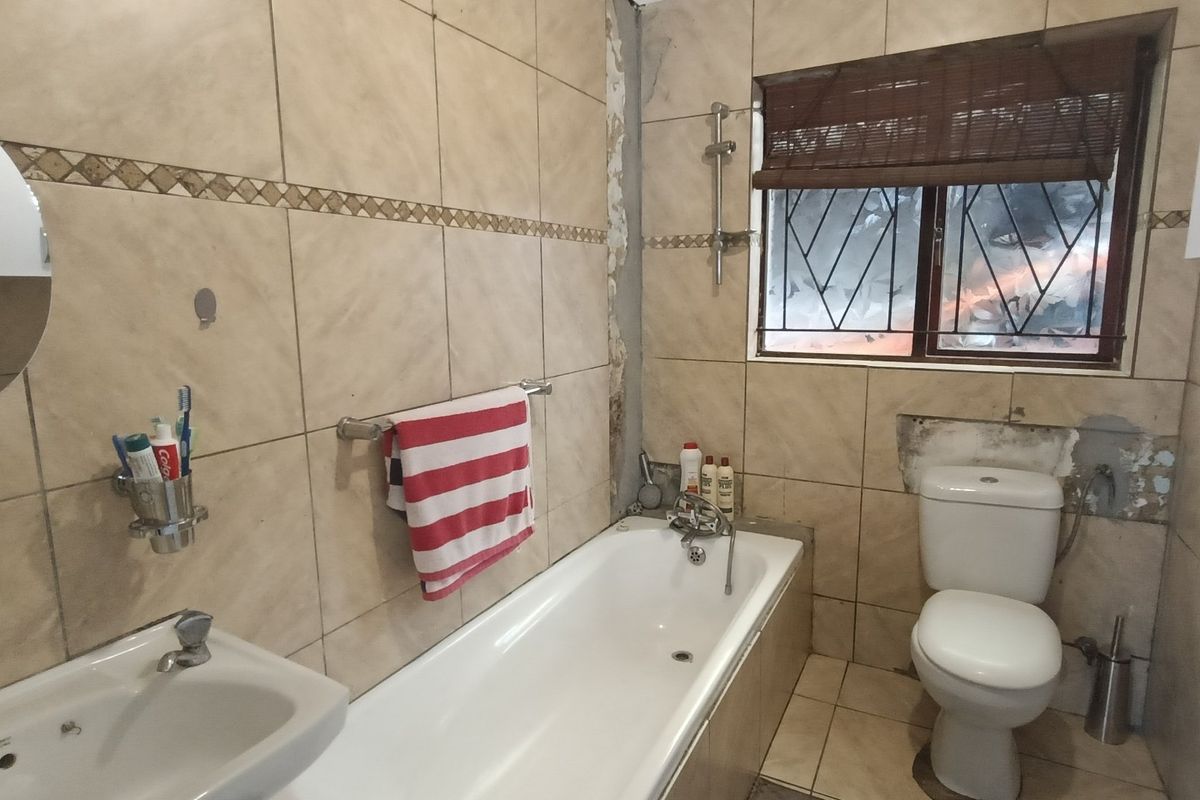 A dated bathroom featuring a bathtub, toilet, and washbasin with tiled finishes, currently requiring repairs to wall plaster and tile work.