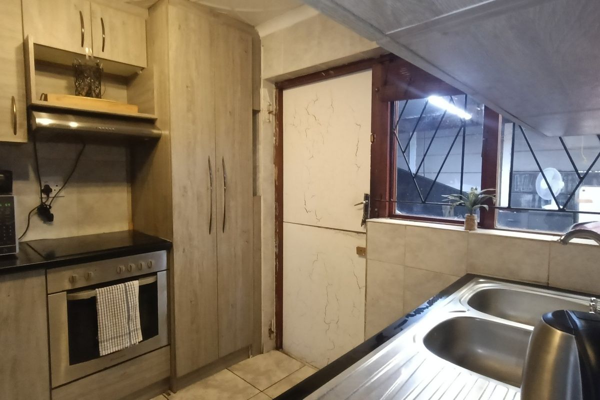 A functional kitchen featuring light wood-look cabinetry, built-in oven with extractor, double sink, and tiled splashbacks, with direct access to an exterior area.