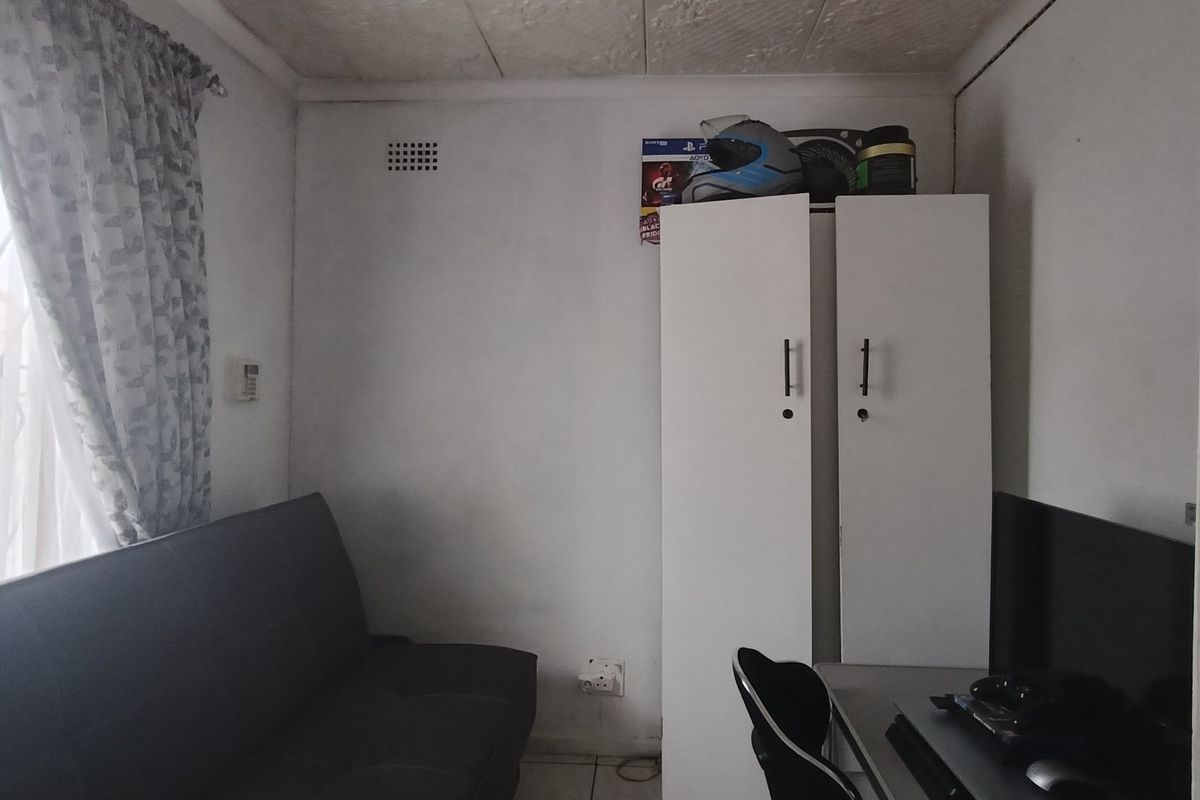A compact bedroom featuring a security gate on the window, ventilation brick, and basic electrical infrastructure.