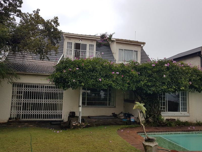 Rear view of a double-story house featuring a balcony, security gates, and a swimming pool with a paved surround.