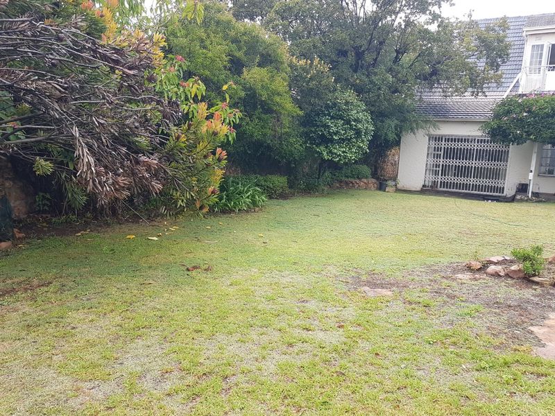 A private rear garden featuring a lawn area, mature trees, and a view of the rear building facade with security gates.