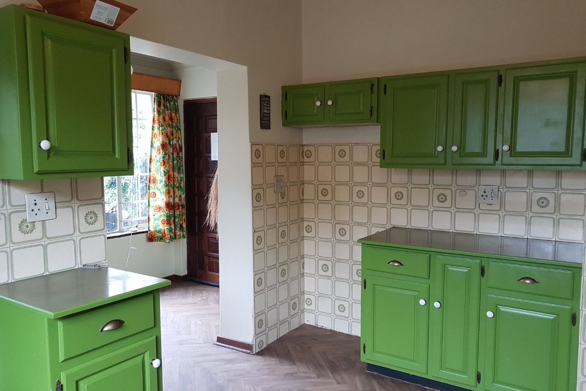 A functional kitchen featuring green cabinetry, tiled backsplash, stainless steel countertops, and parquet flooring, offering a classic layout ready for modernization.