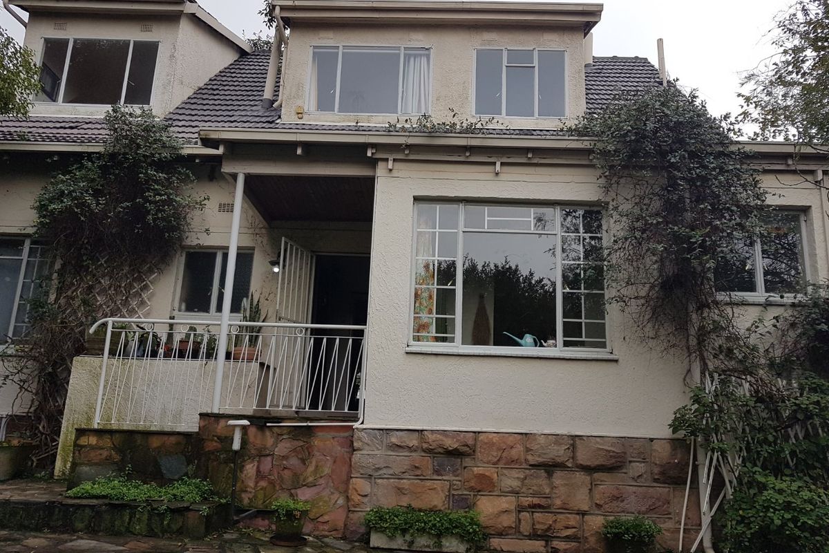 Rear elevation of a multi-story house featuring stone cladding, a tiled roof, and a raised patio area with metal balustrades.