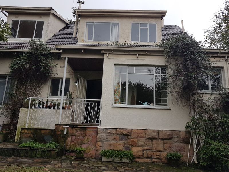 Rear elevation of a multi-story house featuring stone cladding, a tiled roof, and a raised patio area with metal balustrades.