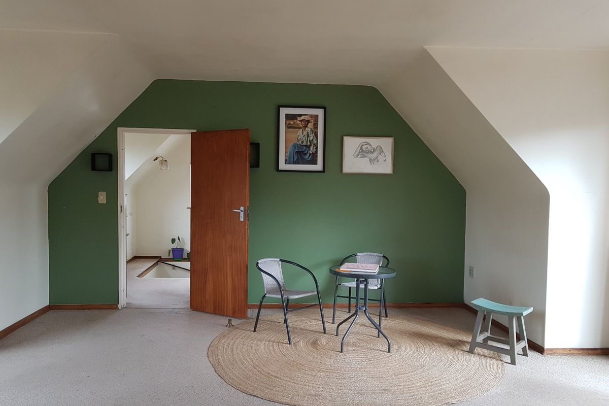 A spacious bedroom featuring sloped ceilings, green accent wall, and carpeted flooring, offering a versatile layout for various furniture arrangements.