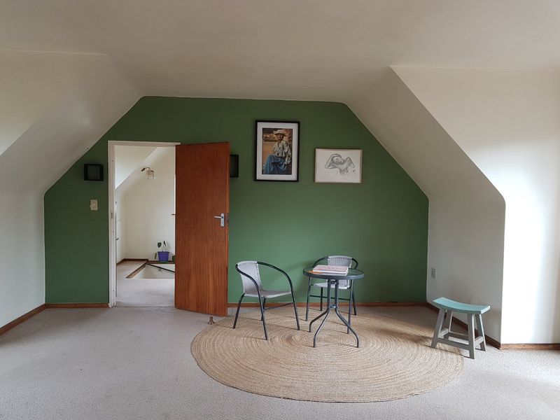 A spacious bedroom featuring sloped ceilings, green accent wall, and carpeted flooring, offering a versatile layout for various furniture arrangements.