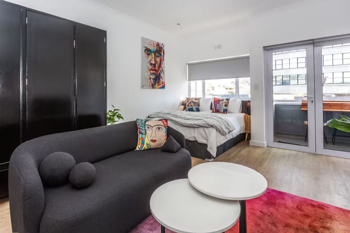 A well-lit bedroom featuring laminate flooring, a built-in wardrobe, and direct access to a private balcony through a glass sliding door.