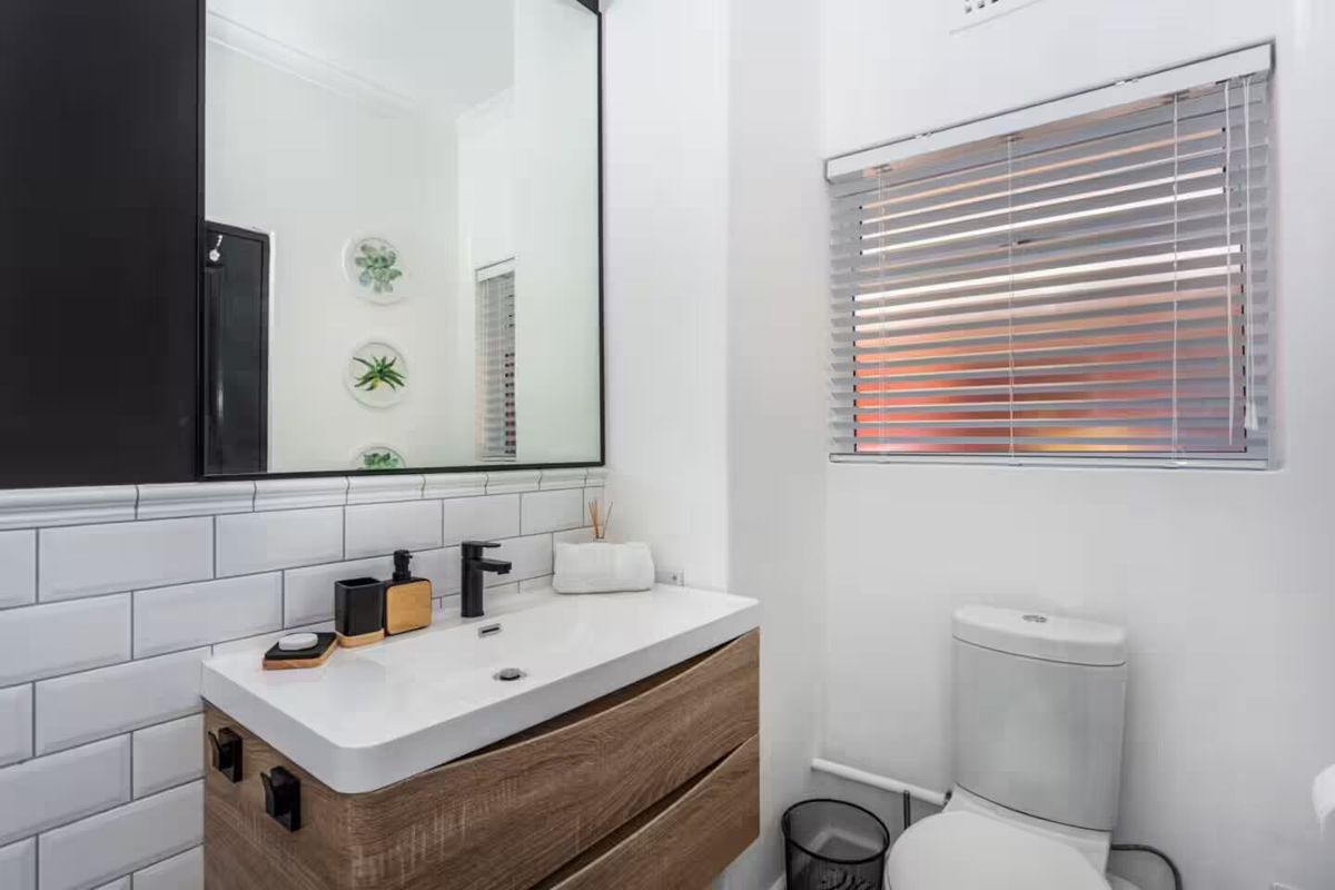 Modern bathroom featuring a wood-finish vanity cabinet, subway tile splashback, large wall-mounted mirror, and a clean white toilet.