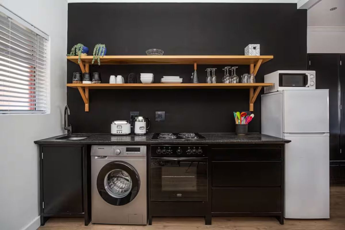 Modern kitchen featuring dark cabinetry, open timber shelving, built-in oven, gas hob, and integrated sink with a sleek black finish.
