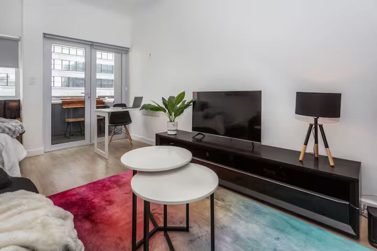 A bright living room featuring laminate flooring and a double glass door leading to a balcony, providing natural light and access to outdoor space.
