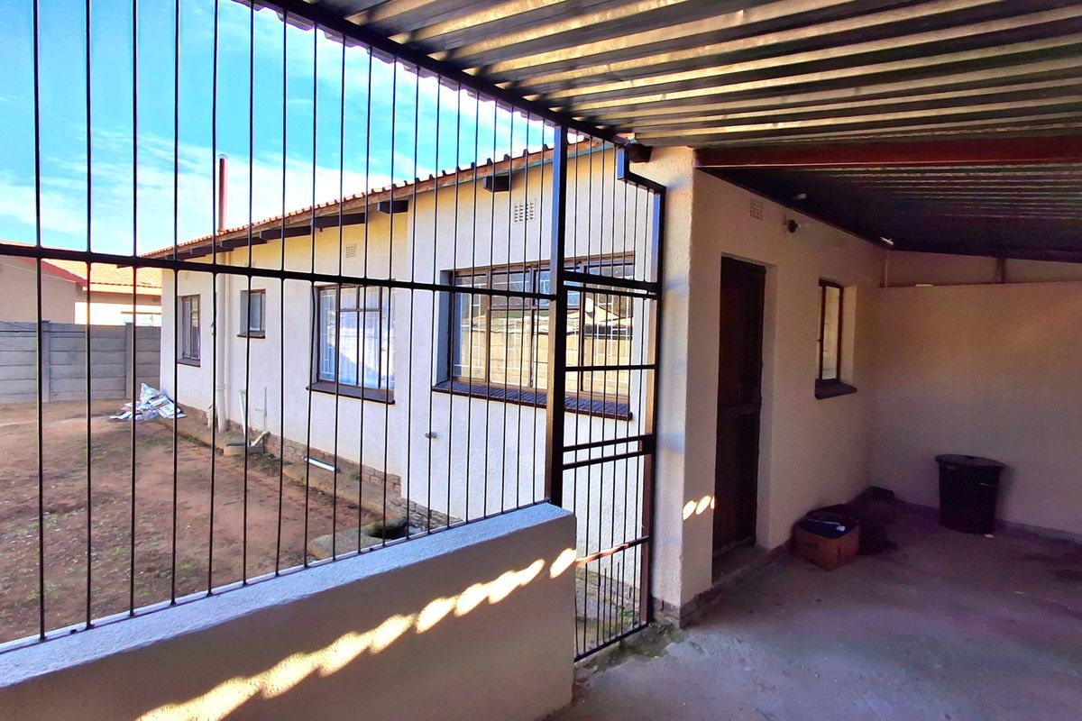 Rear exterior view of the property featuring a covered patio area, security bars, and a fenced yard space.