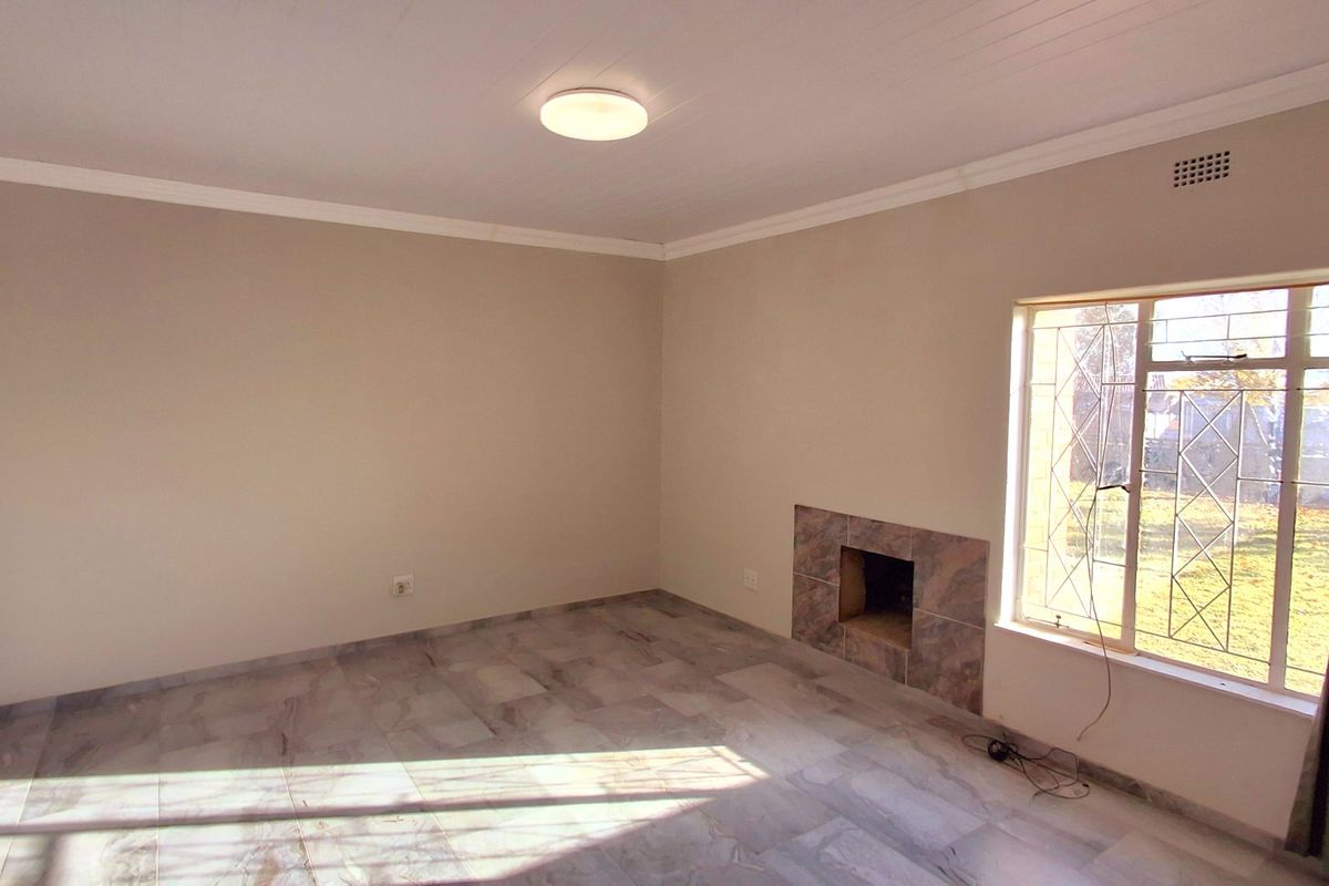 A bright, empty living room featuring tiled flooring, a built-in fireplace, and large windows with security bars.