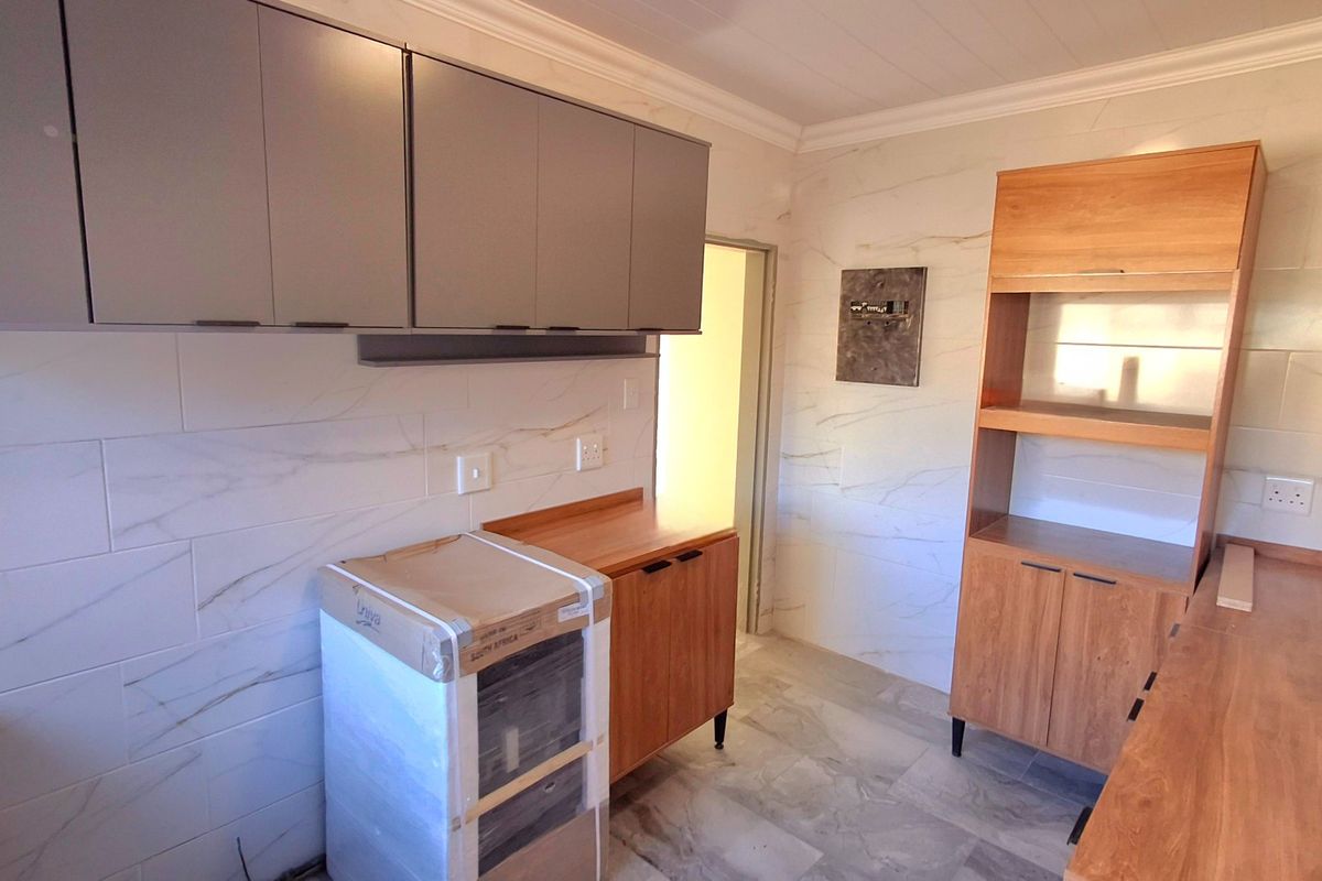 A modern, empty kitchen featuring marble-look wall and floor tiles, wooden countertops, and ample built-in cabinetry.