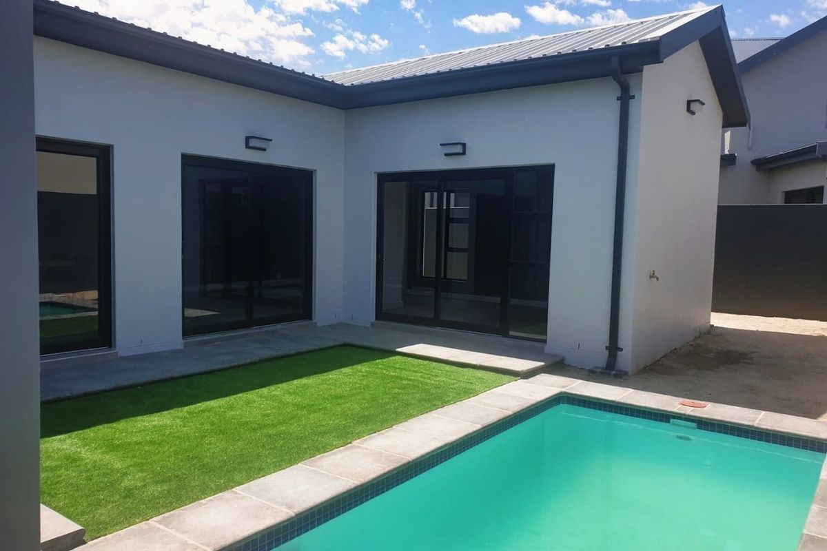 A modern rear courtyard featuring a swimming pool, artificial lawn, and large sliding glass doors providing seamless indoor-outdoor flow.