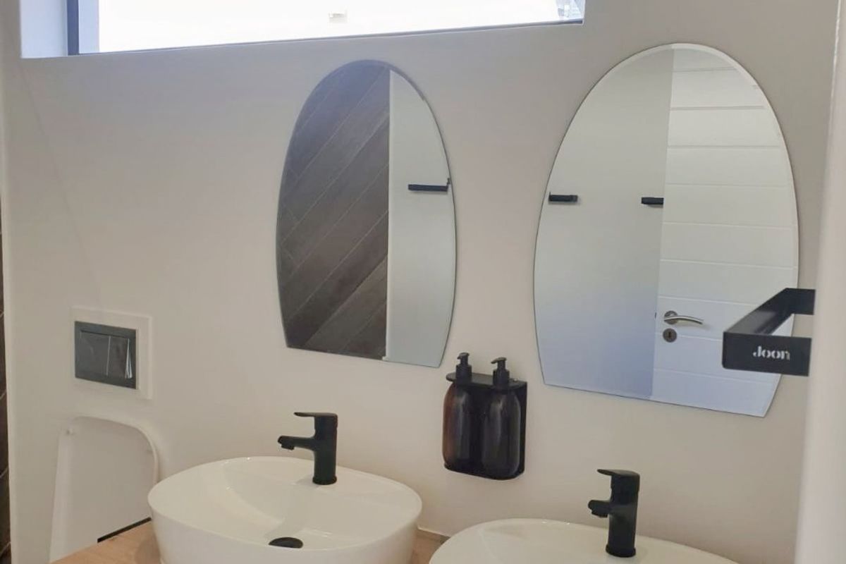 Modern bathroom featuring a double vanity with vessel sinks, matte black fixtures, arch mirrors, and a wall-mounted toilet under a clerestory window.