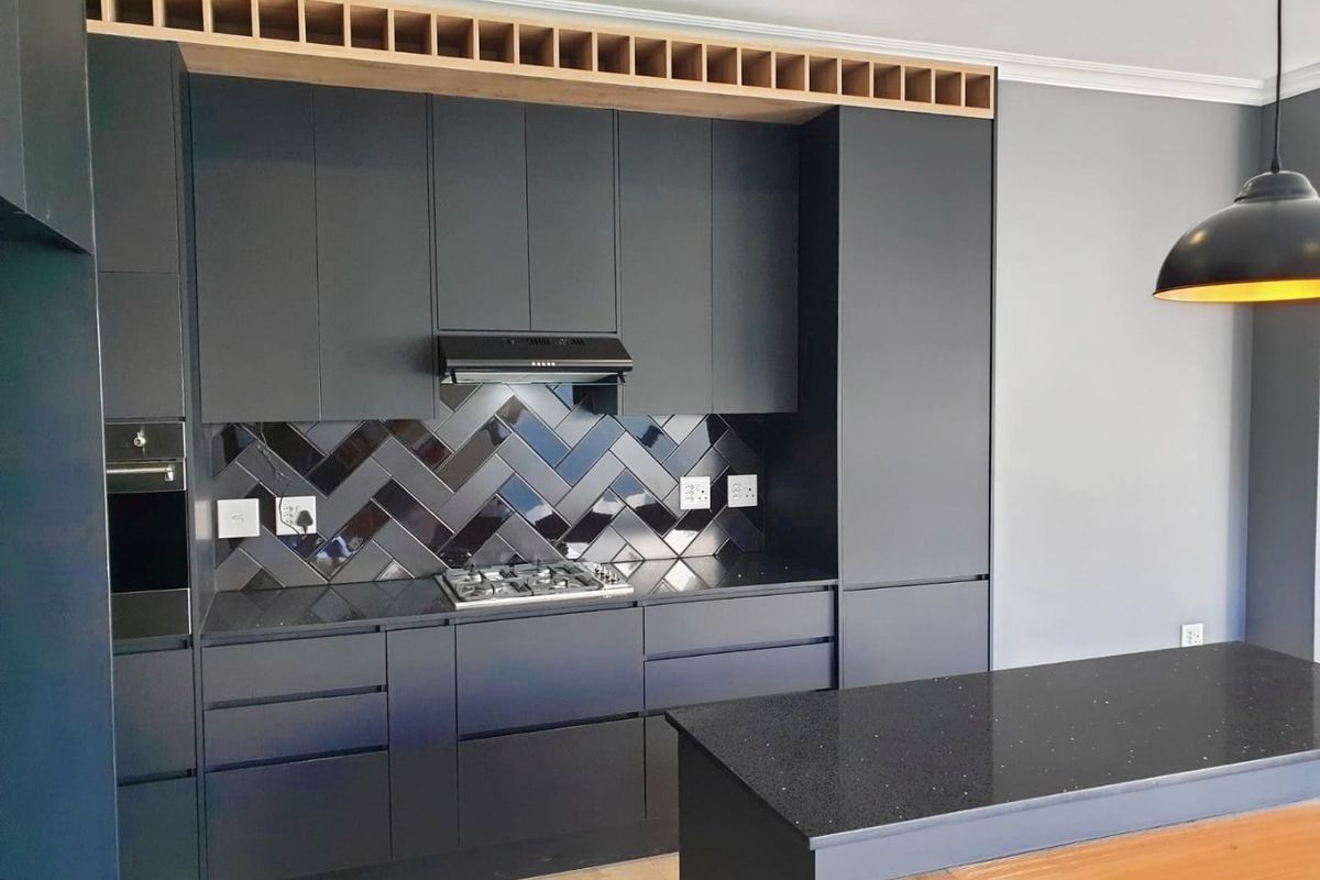 Modern kitchen featuring dark matte cabinetry, a herringbone tile backsplash, stone countertops, integrated appliances, and a functional kitchen island.