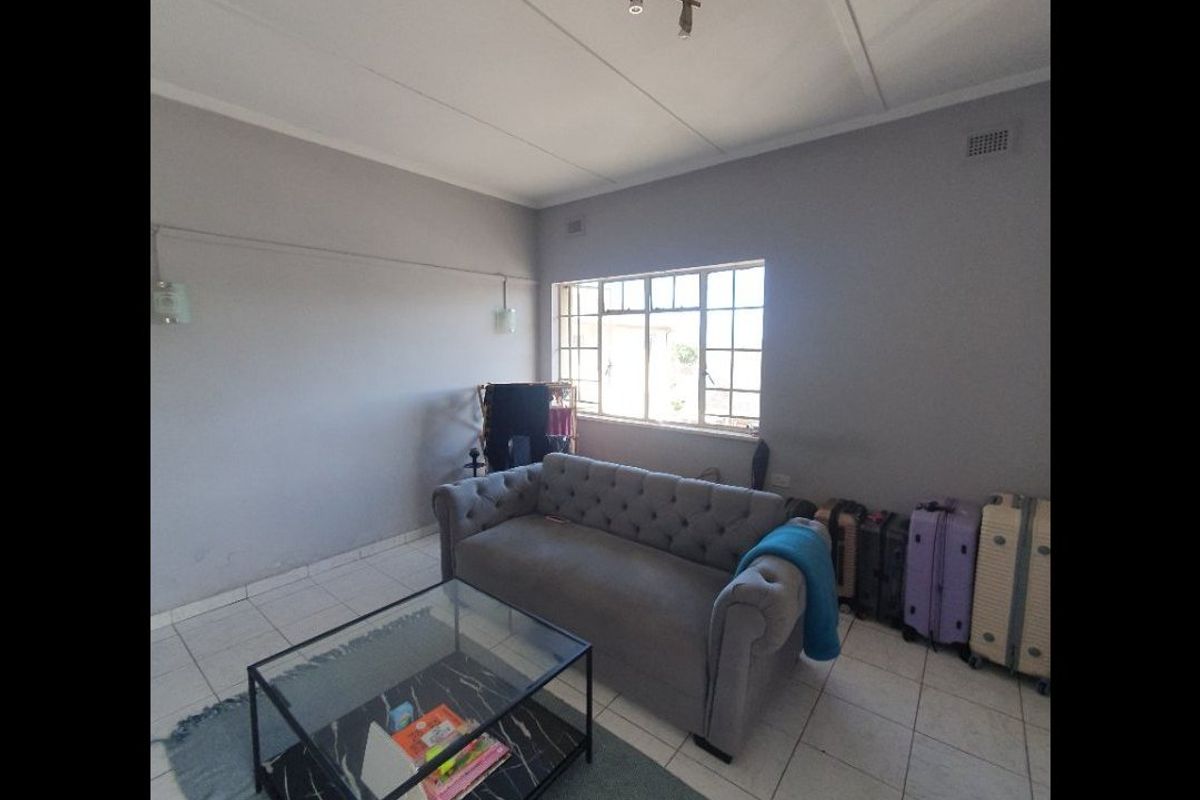 A living room featuring tiled flooring, neutral wall finishes, and a steel-framed window providing natural light.