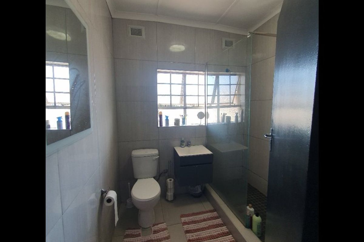 A functional bathroom featuring tiled walls and flooring, a vanity unit, a toilet, and a glass-enclosed shower area.