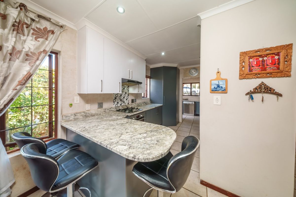 A functional kitchen featuring granite countertops, built-in cabinetry, a gas hob with extractor fan, and tiled flooring, with an adjacent scullery area.