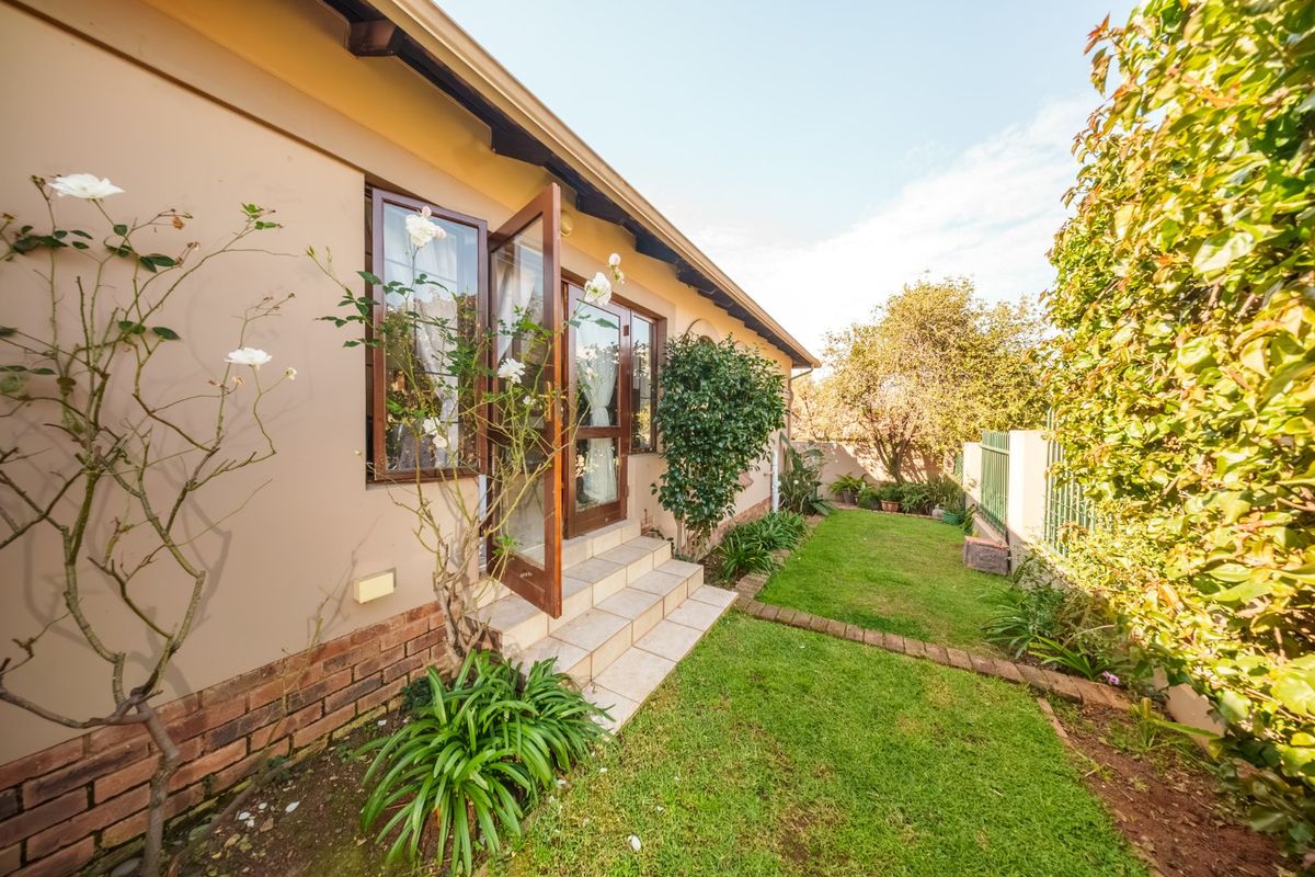 A well-maintained rear garden area featuring a lawn, established landscaping, and direct access to the home via tiled steps and timber-framed glass doors.
