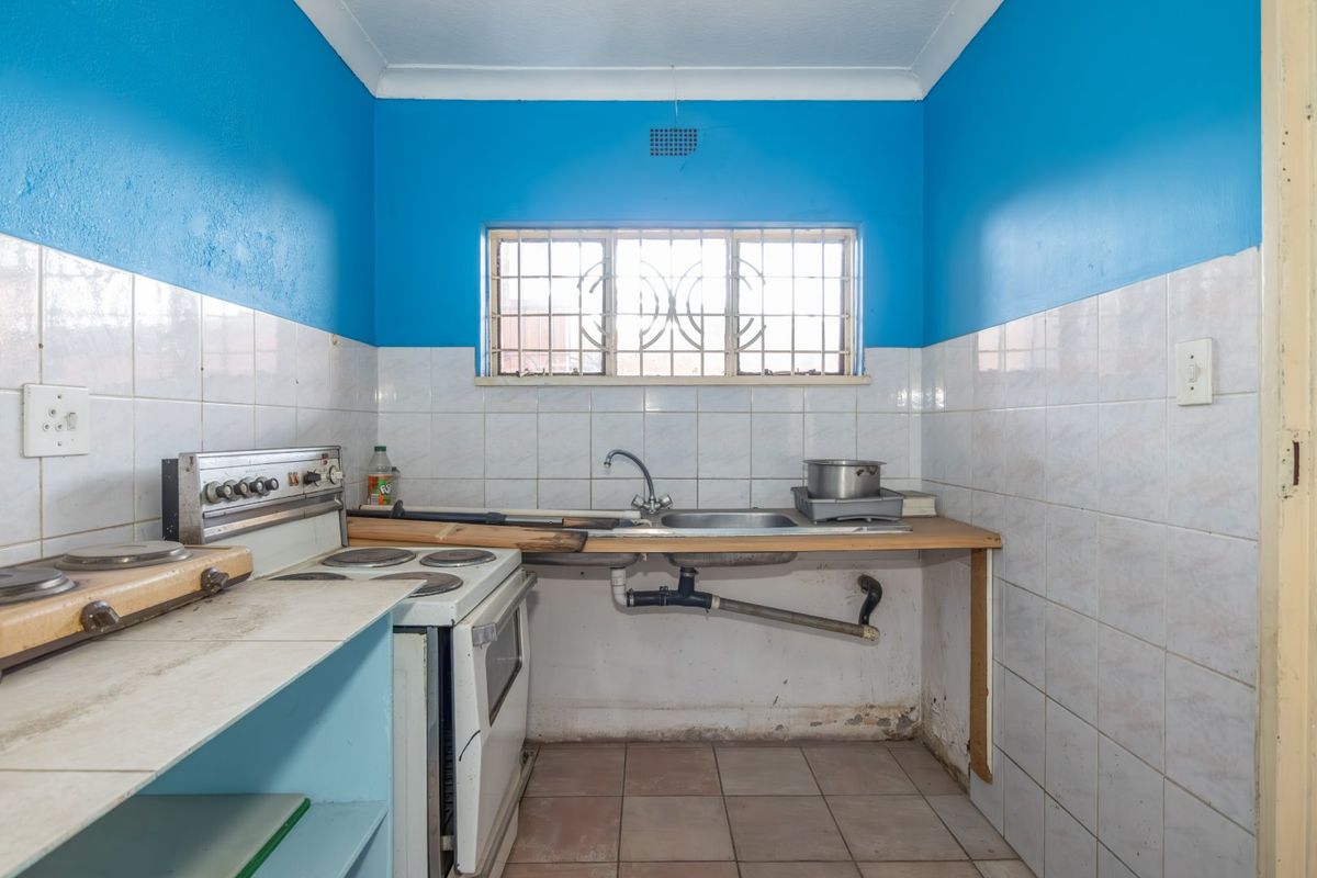 A compact kitchen featuring a stainless steel sink, tiled splashback, and a freestanding stove, requiring cosmetic updates and repairs to the cabinetry and plumbing.