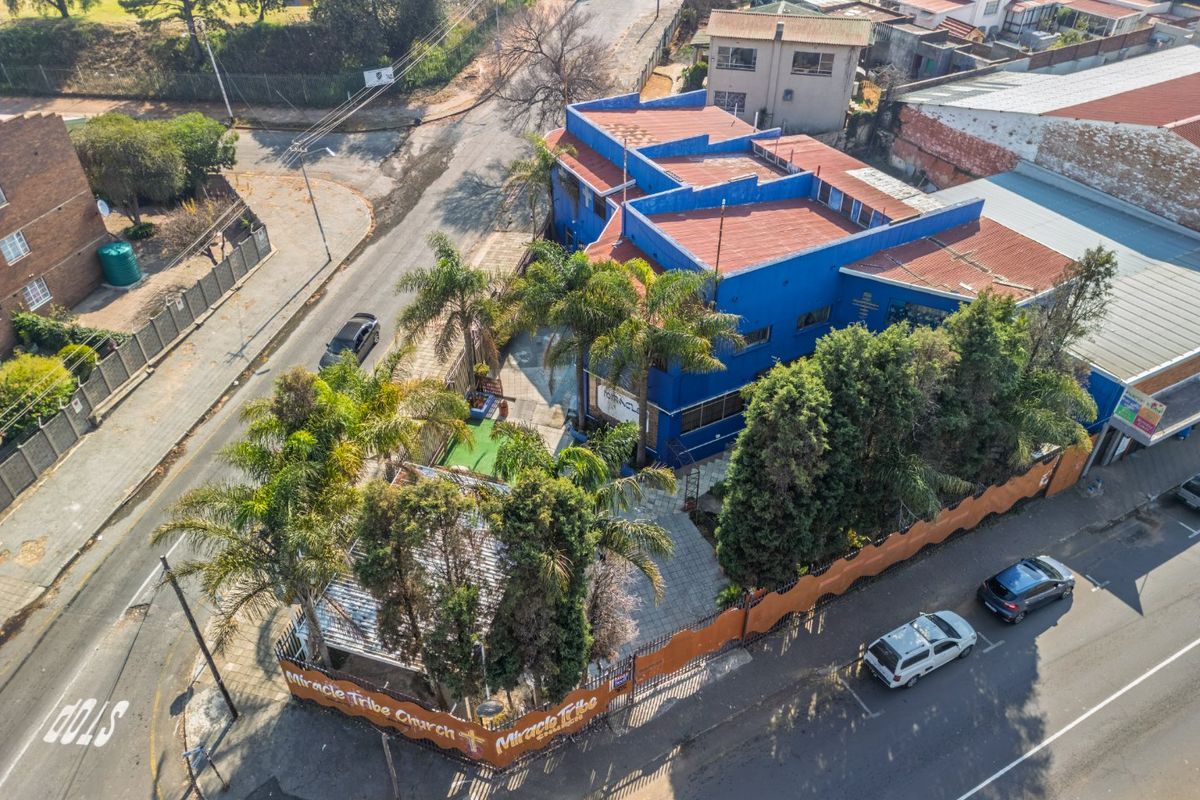 Aerial view of a commercial property featuring a blue building, paved courtyard, and perimeter security fencing situated on a corner lot.