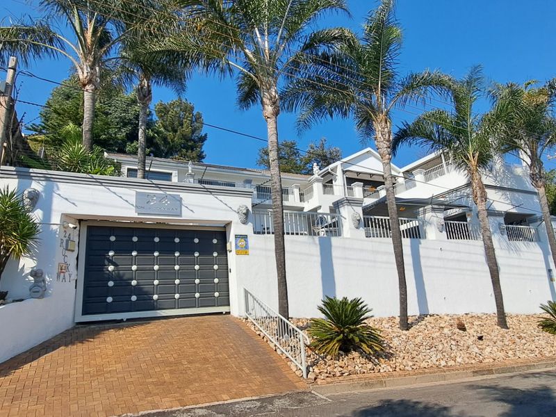 Front elevation of a multi-level residence featuring a paved driveway, automated garage door, and established palm trees along the street-facing boundary.