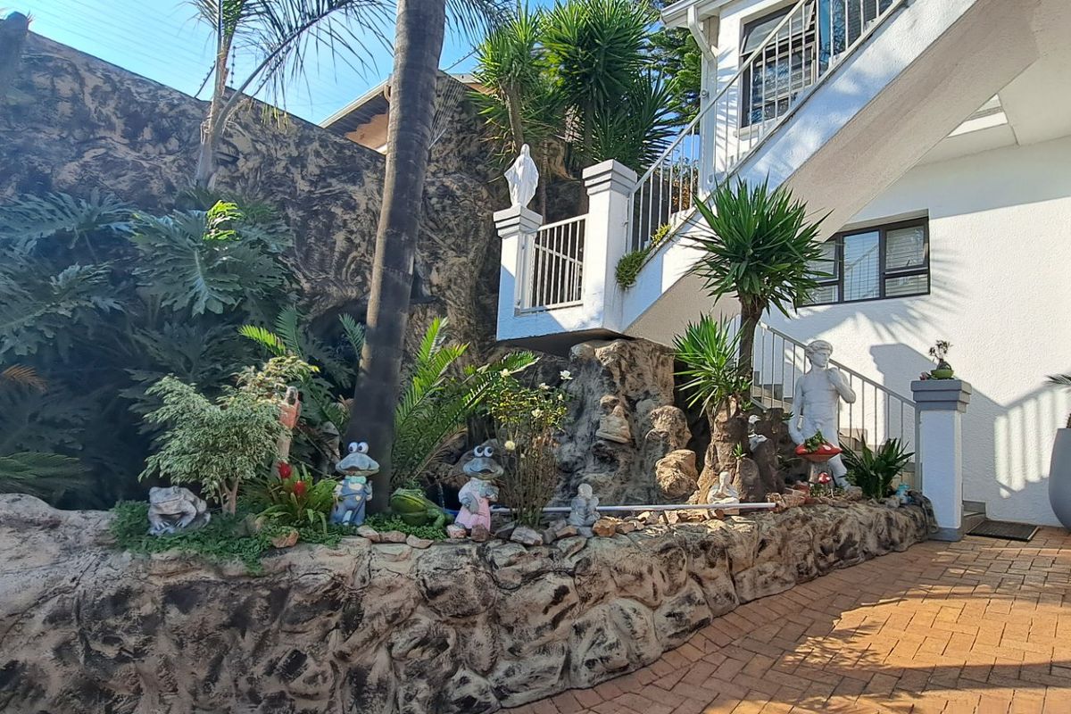 A landscaped rear garden area featuring a stone retaining wall, paved patio, and an external staircase leading to the upper level of the house.