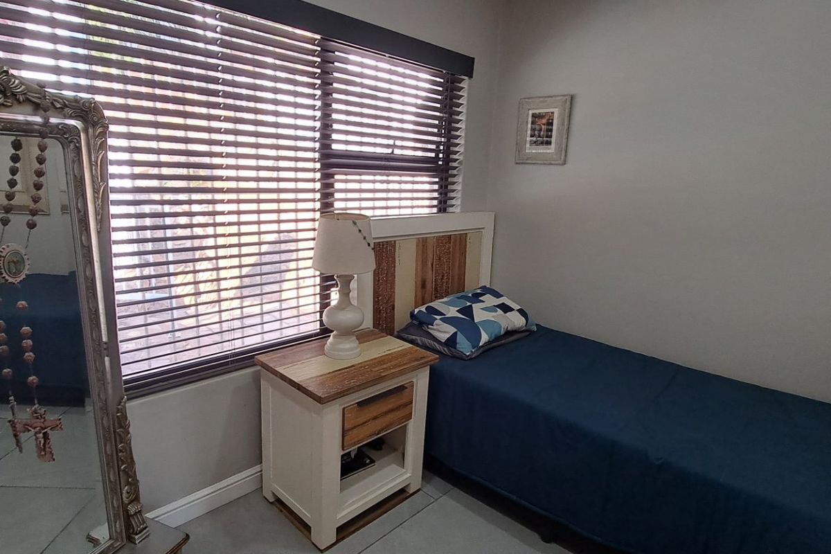 A compact bedroom featuring neutral wall tones, tiled flooring, and large windows fitted with venetian blinds for adjustable natural light.