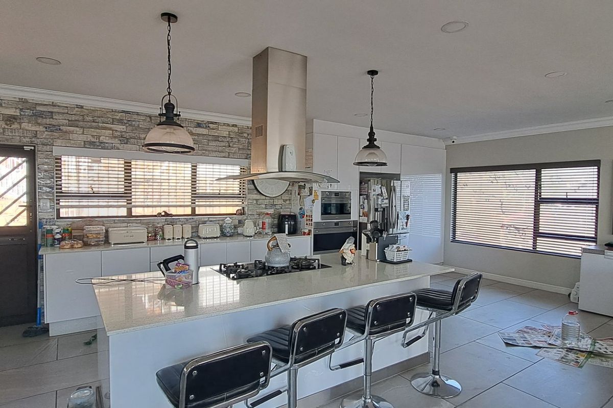Modern kitchen featuring a central island with gas hob, stone countertops, built-in appliances, and tiled flooring, offering a functional and open layout.