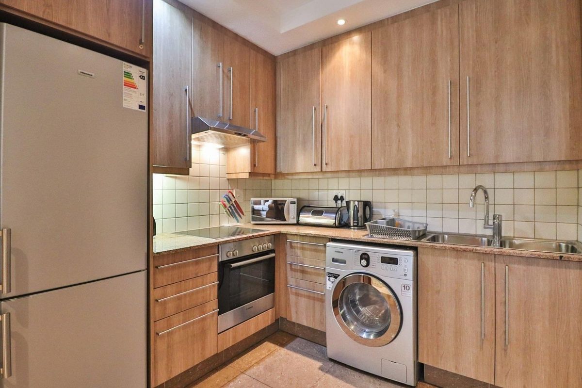 A functional kitchen featuring light wood-finish cabinetry, granite countertops, tiled backsplash, and integrated appliances including an oven, hob, and extractor fan.