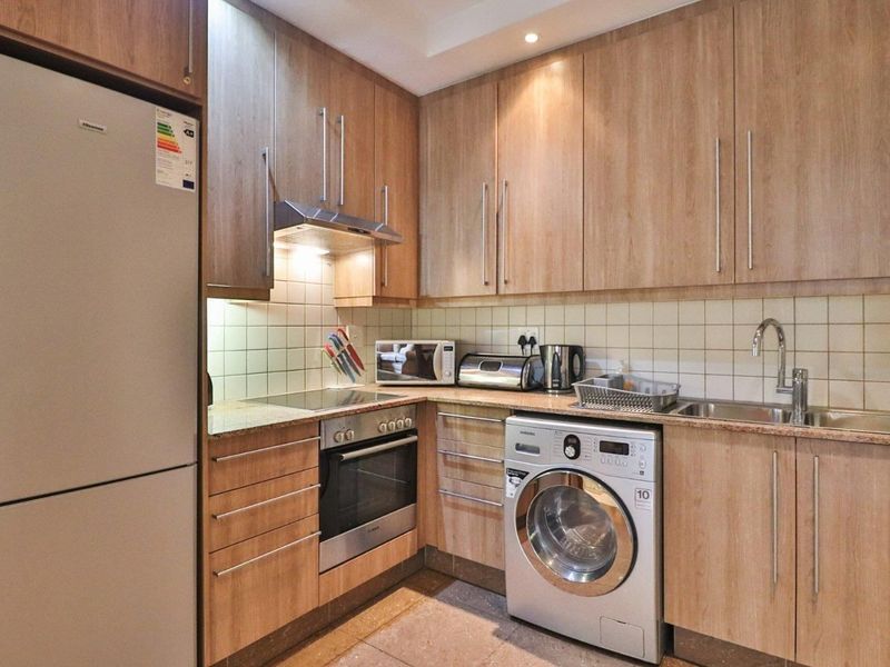 A functional kitchen featuring light wood-finish cabinetry, granite countertops, tiled backsplash, and integrated appliances including an oven, hob, and extractor fan.